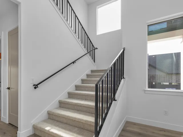 Striking staircase featuring light-finish treads, black metal railings with handrails, and abundant natural light from overhead windows