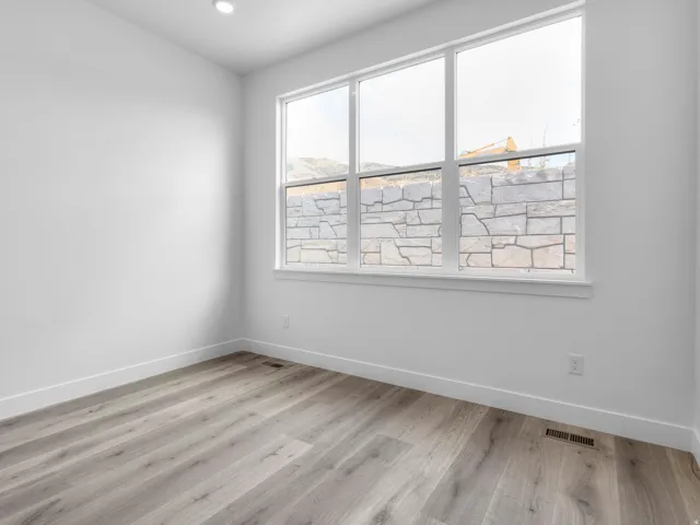 Bright interior space featuring a large three-pane window with white trim, wood-finish flooring, and crisp white walls