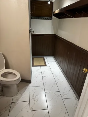 Half bath featuring light marble finish flooring, wooden walls, and wainscoting