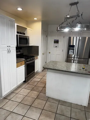 Kitchen featuring stainless steel appliances, white cabinetry, tasteful backsplash, dark countertops, and decorative light fixtures