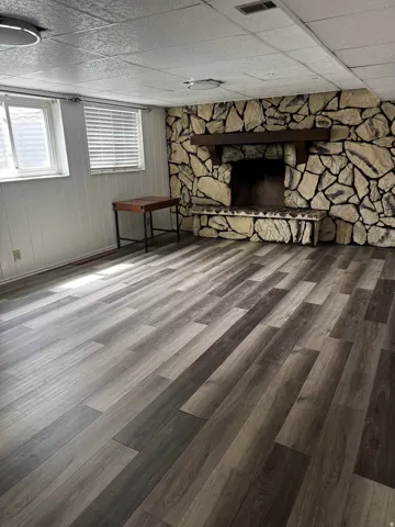 Below grade area with a drop ceiling, a stone fireplace, and dark wood finished floors