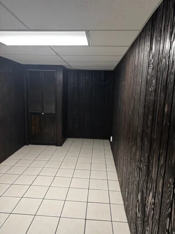 Spare room with a paneled ceiling, light tile patterned floors, and wooden walls