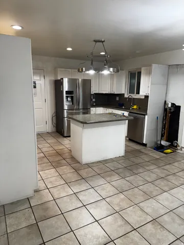 Kitchen featuring stainless steel appliances, a kitchen island, white cabinets, decorative backsplash, and decorative light fixtures