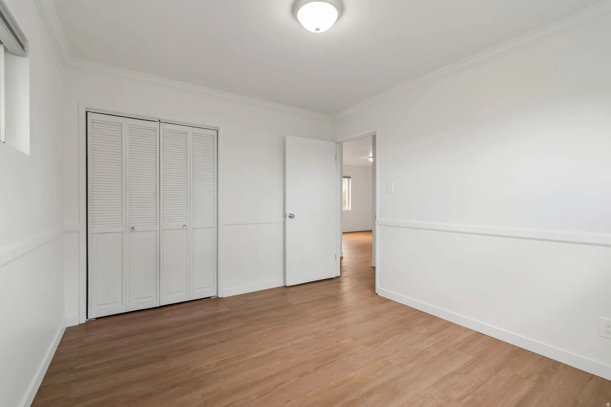 Unfurnished bedroom with light wood-style flooring, ornamental molding, and a closet