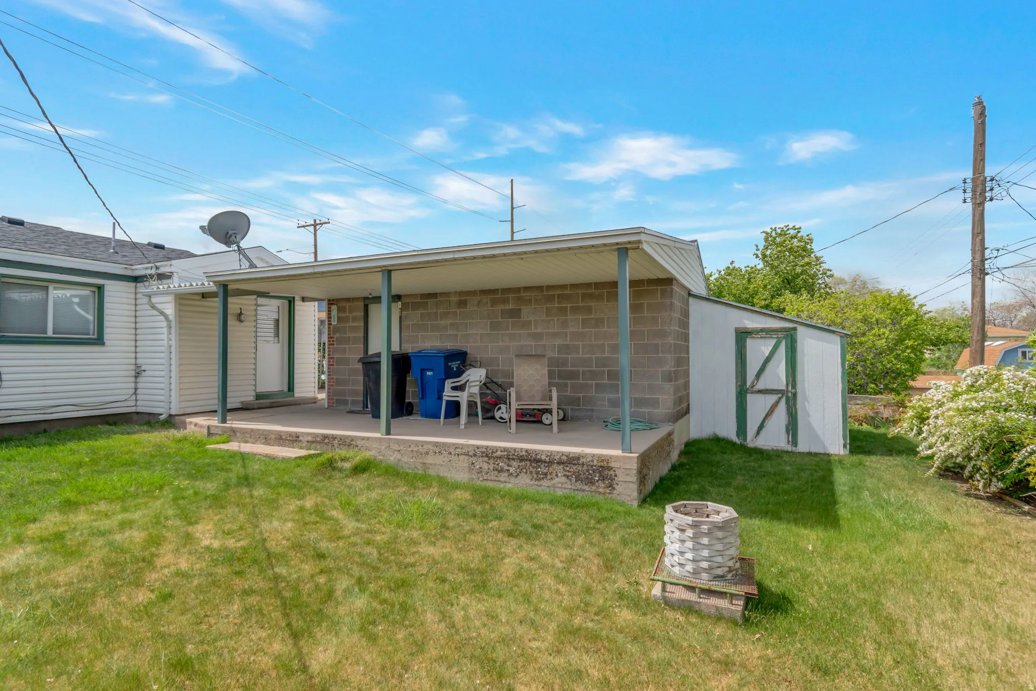 Back of house featuring a shed, a lawn, concrete block siding, and a patio