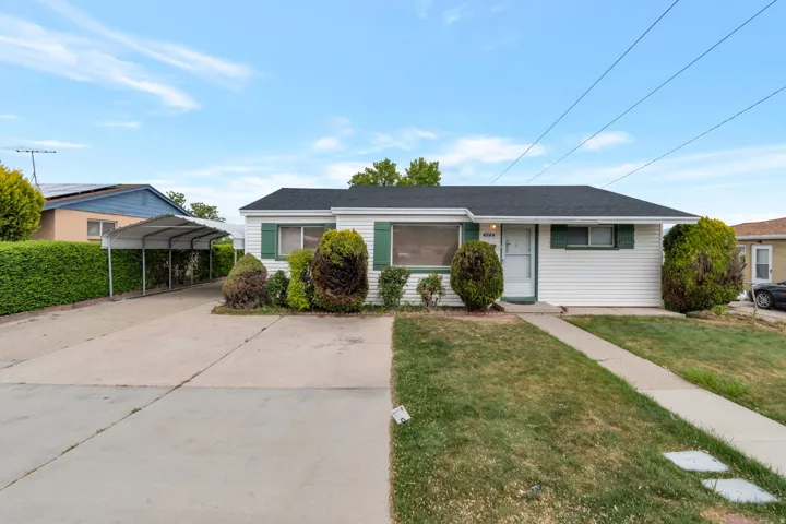 View of front of property with a front yard, a shingled roof, concrete driveway, and a detached carport