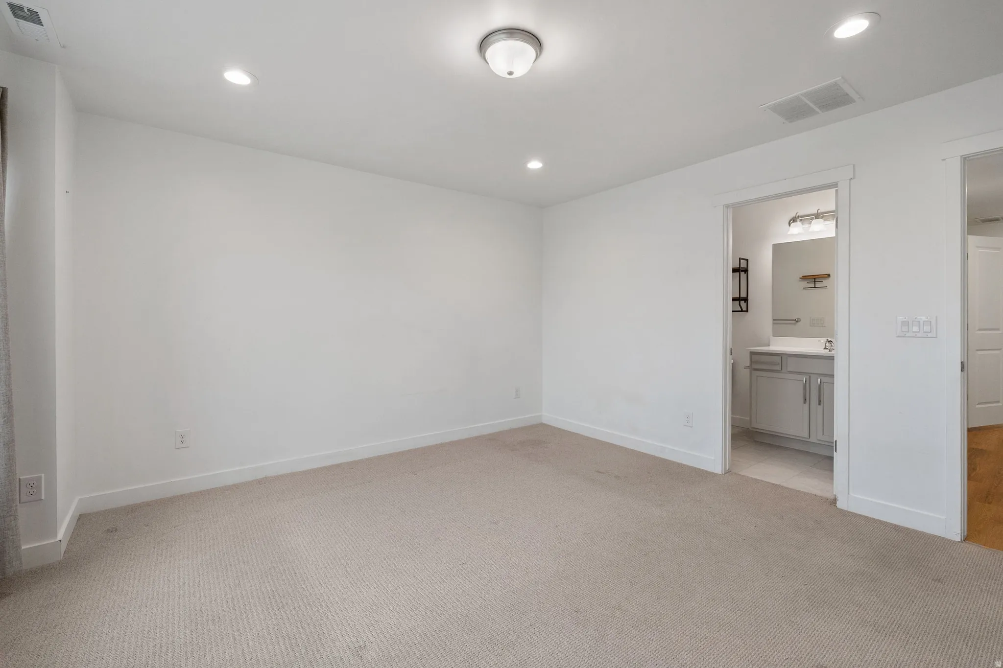 Unfurnished bedroom with light carpet, recessed lighting, and ensuite bathroom