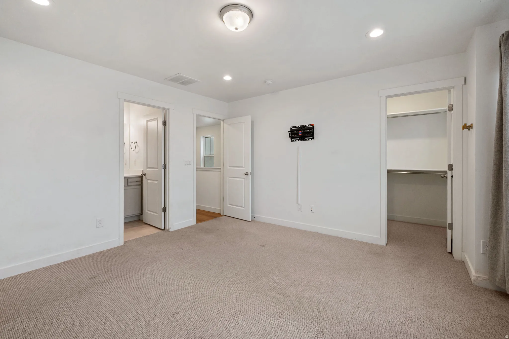 Unfurnished bedroom featuring a walk in closet, light carpet, recessed lighting, and connected bathroom