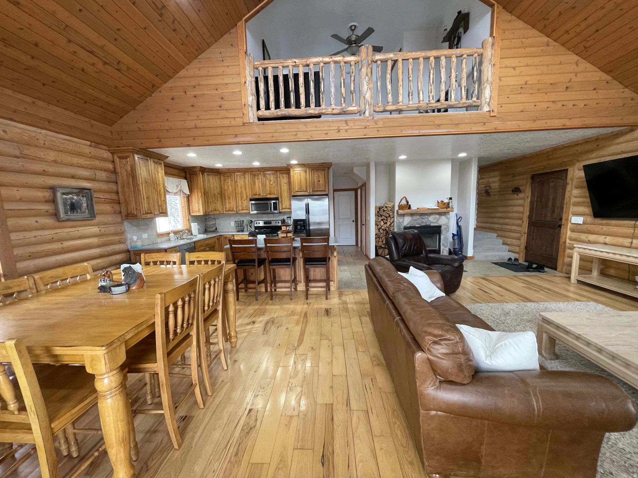 Dining area featuring rustic walls, a vaulted wooden ceiling, a fireplace, light wood finished floors, and a ceiling fan
