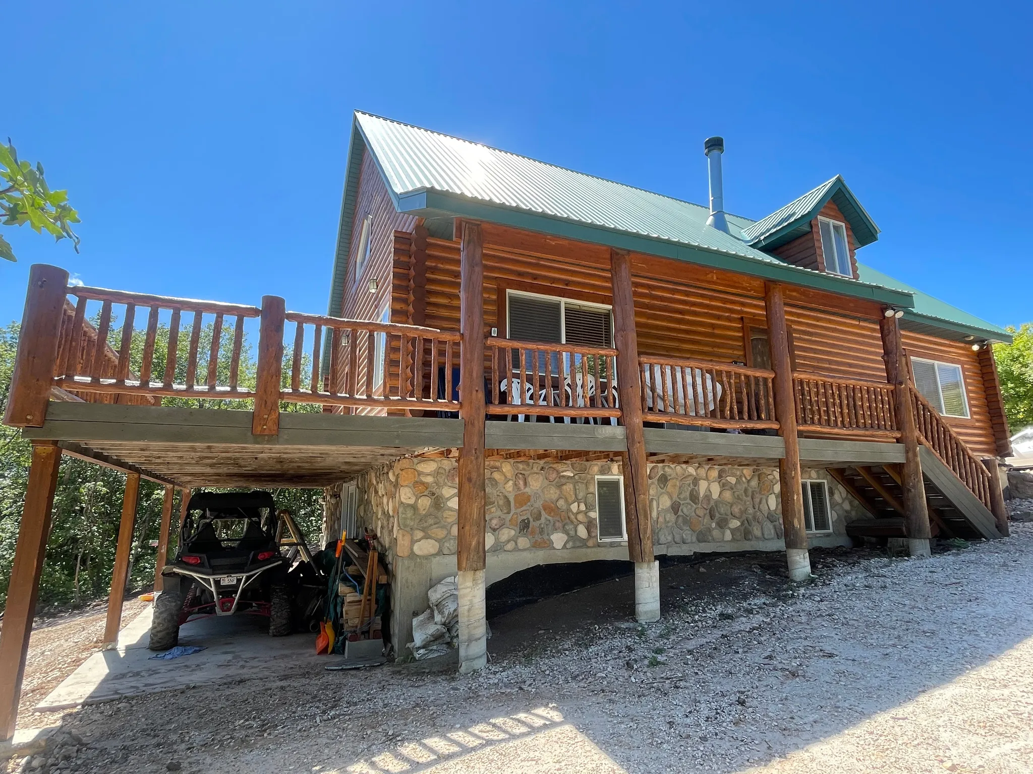 Back of property featuring a metal roof, stone siding, covered porch, and a carport