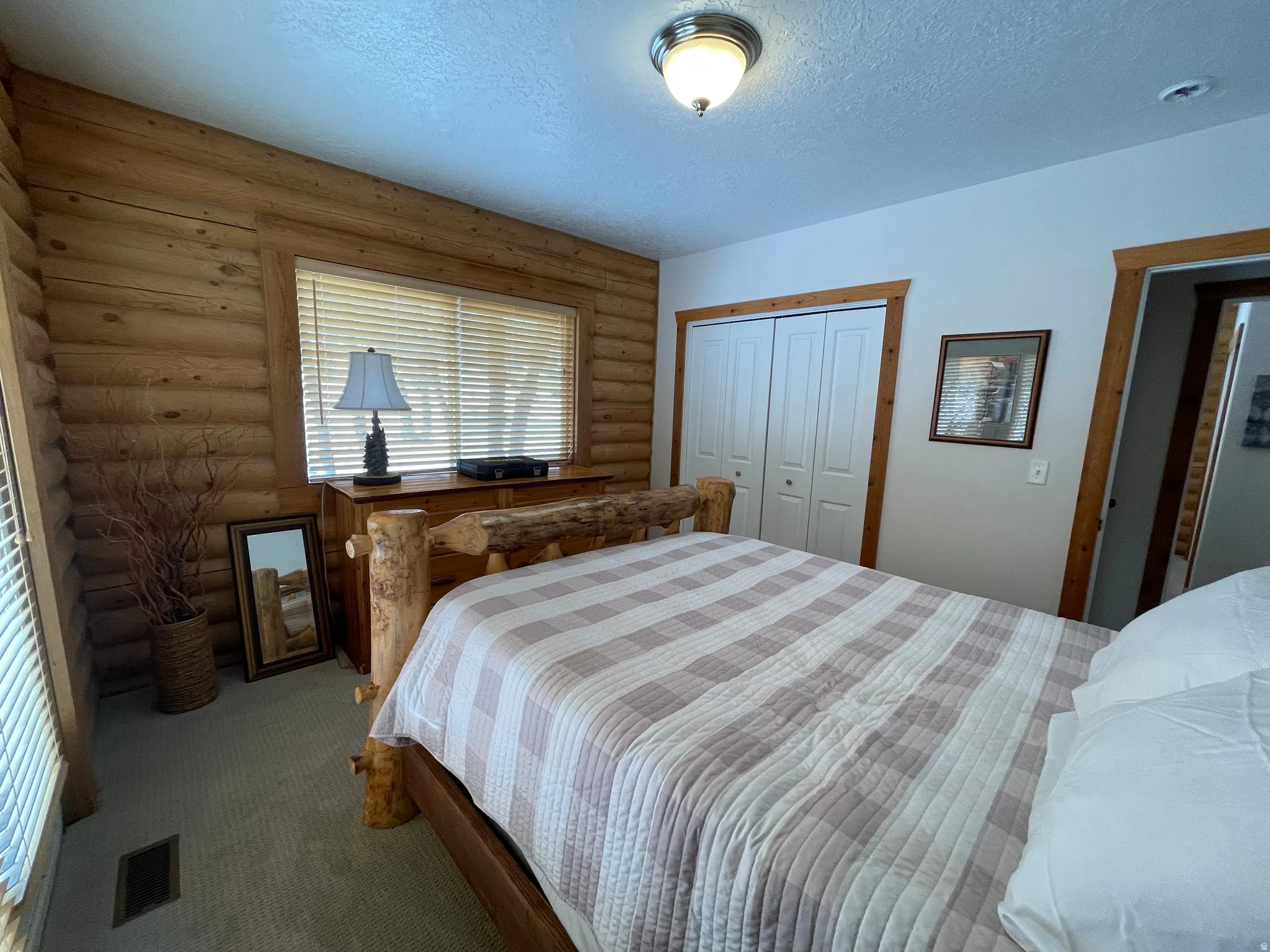 Bedroom featuring log walls, dark carpet, a textured ceiling, and a closet