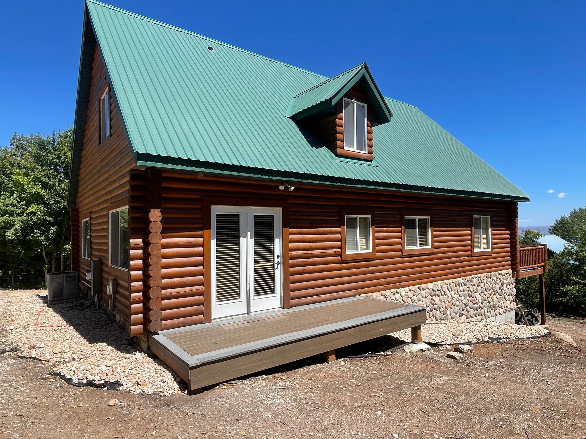 Rear view of house featuring stone siding, a metal roof, and a deck