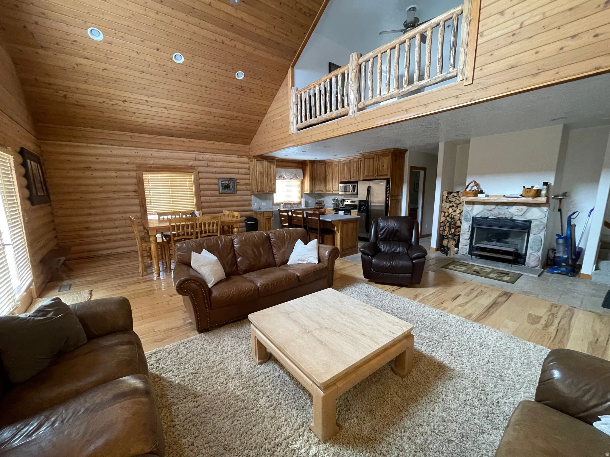 Living room featuring a fireplace, rustic walls, light wood-style floors, a vaulted wood ceiling, and ceiling fan