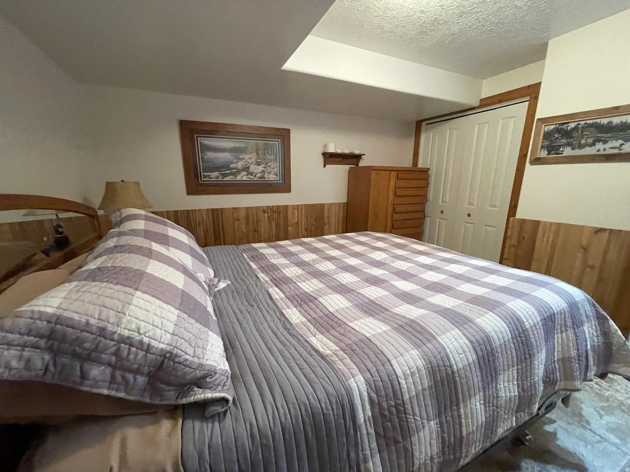 Bedroom with wood walls, a closet, a wainscoted wall, and a textured ceiling