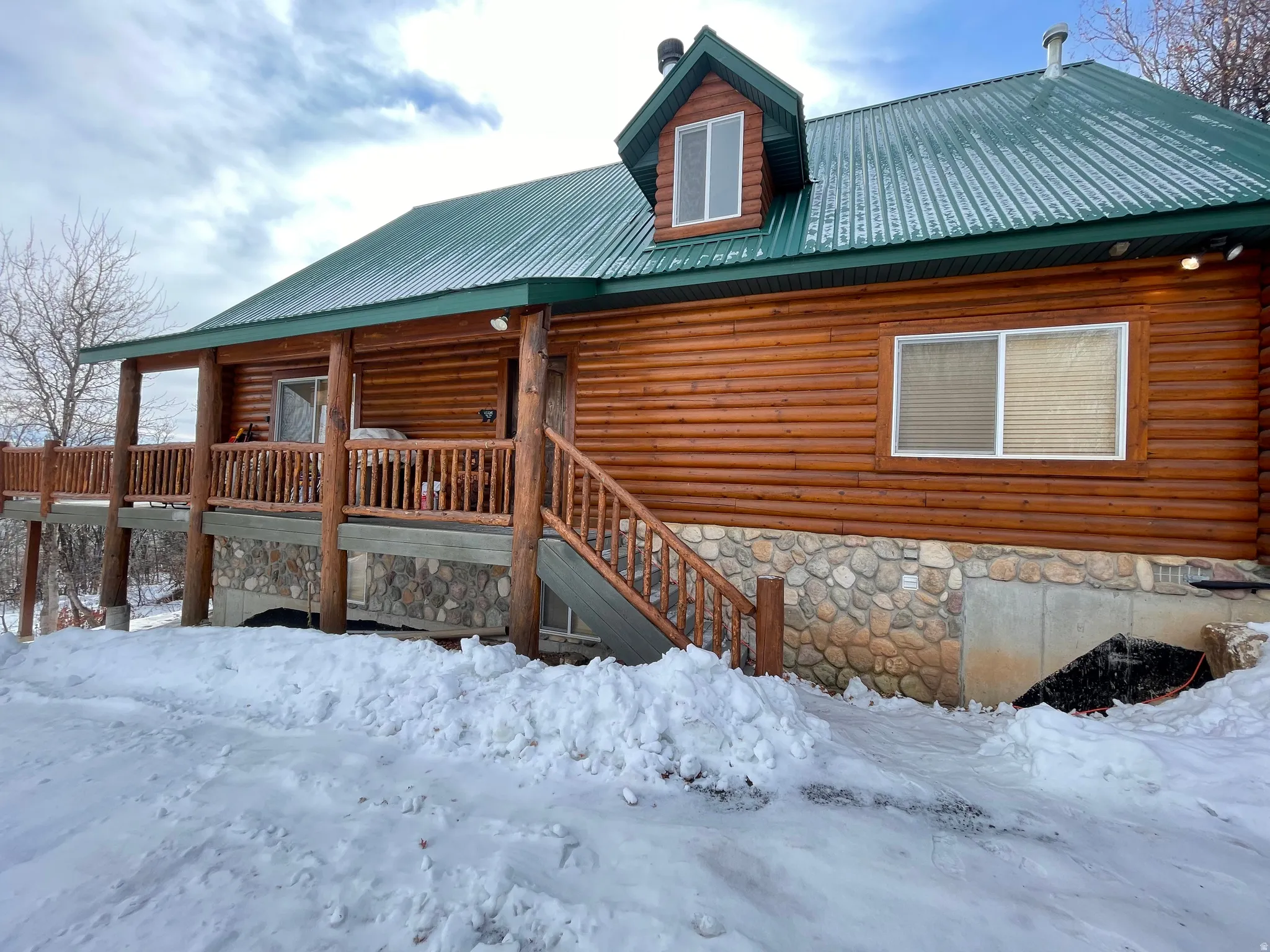 View of front of home with a metal roof, stone siding, and covered porch