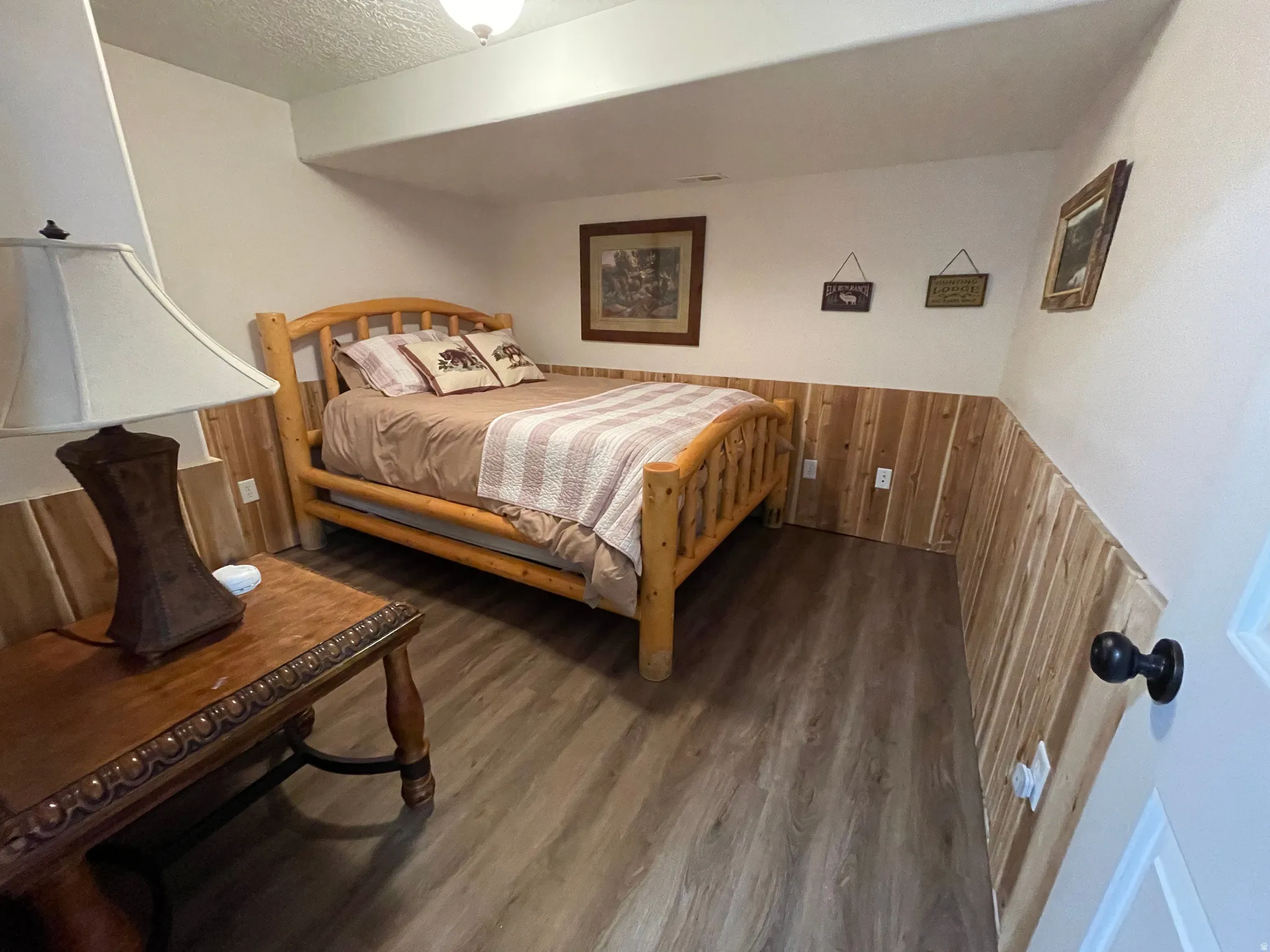 Bedroom featuring wood walls, wainscoting, a textured ceiling, and dark wood-style flooring