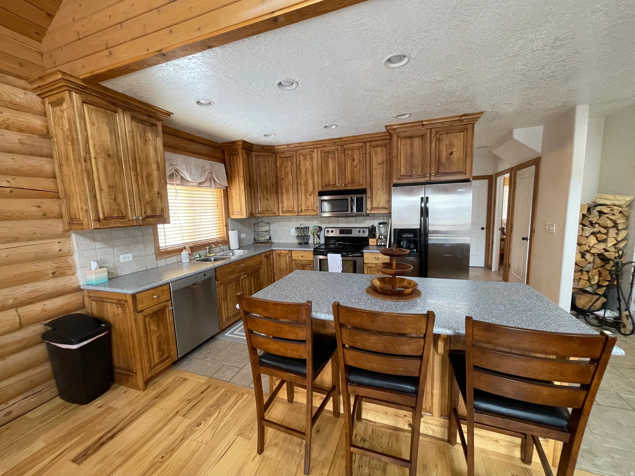Kitchen featuring decorative backsplash, wood finish cabinets, stainless steel appliances, a breakfast bar area, and light wood-style floors