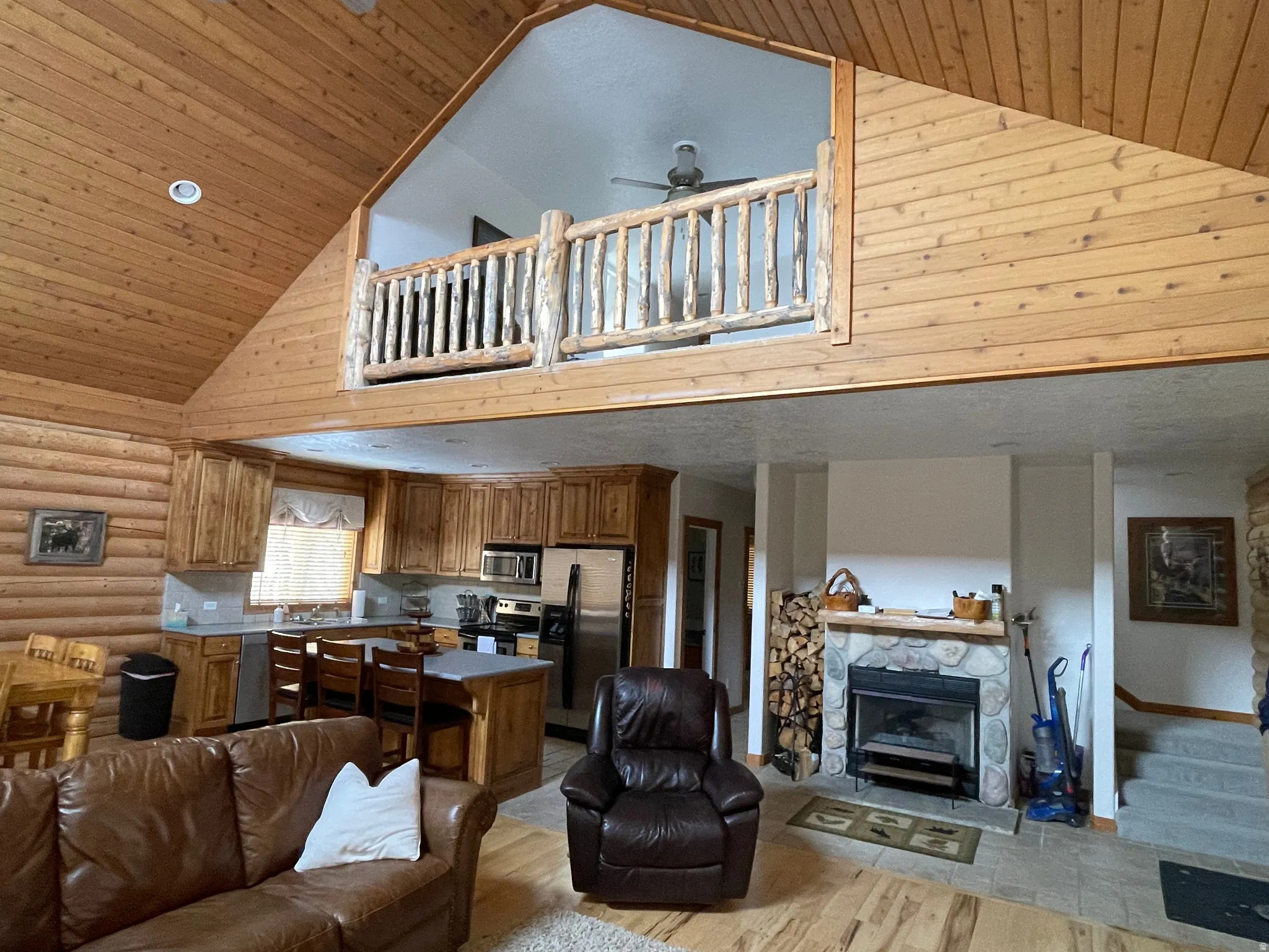 Living area featuring a vaulted wooden ceiling, log walls, a fireplace, light wood-style flooring, and ceiling fan