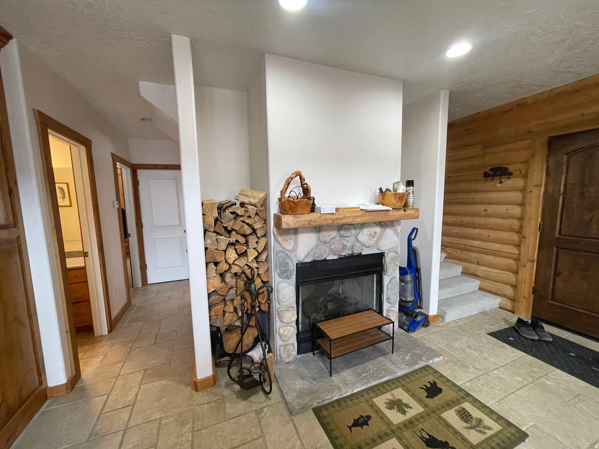 Living room featuring a stone fireplace, stone tile flooring, a textured ceiling, and rustic walls
