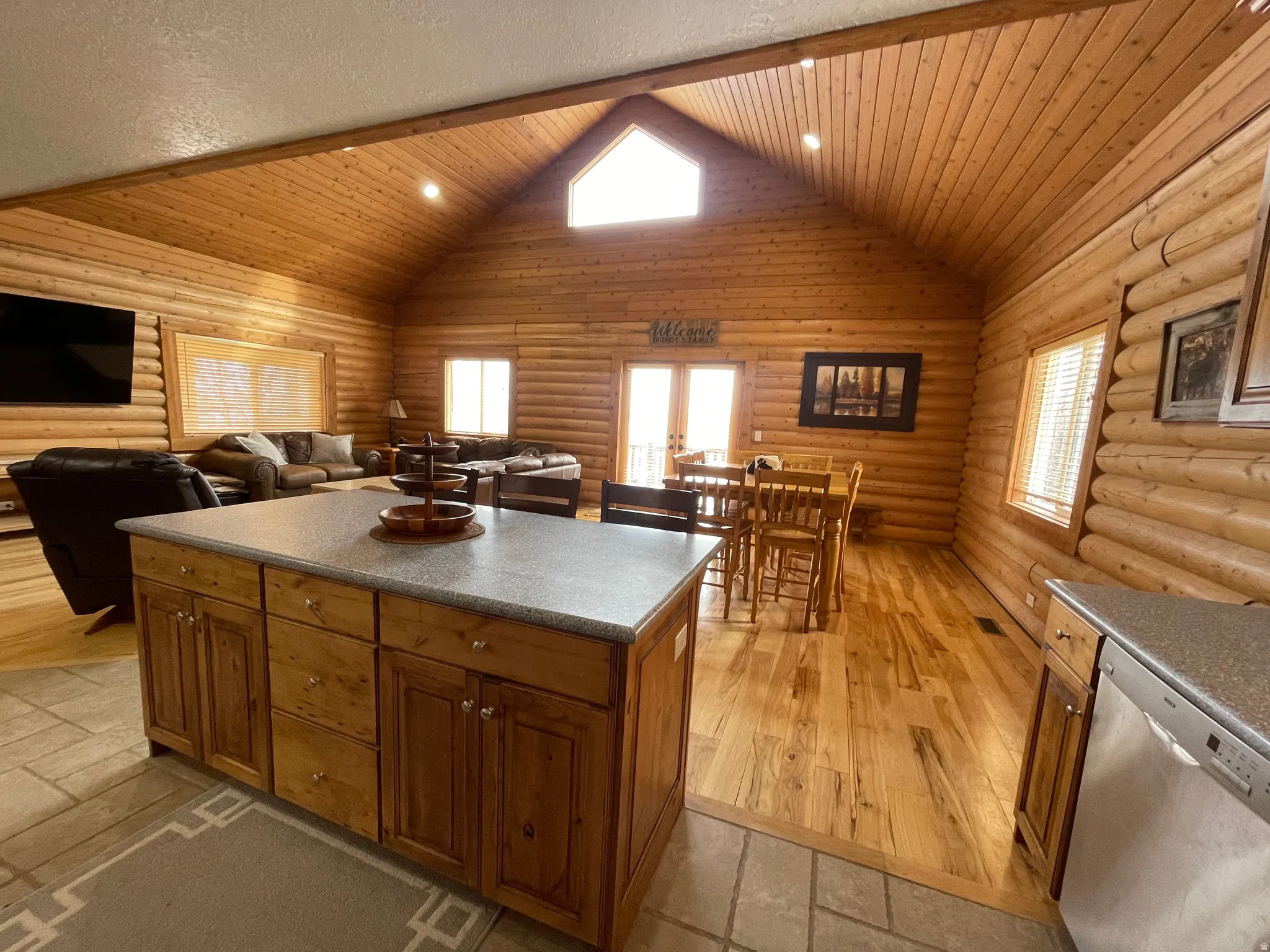 Kitchen featuring log walls, dishwasher, a center island, wood finish cabinetry, and open floor plan