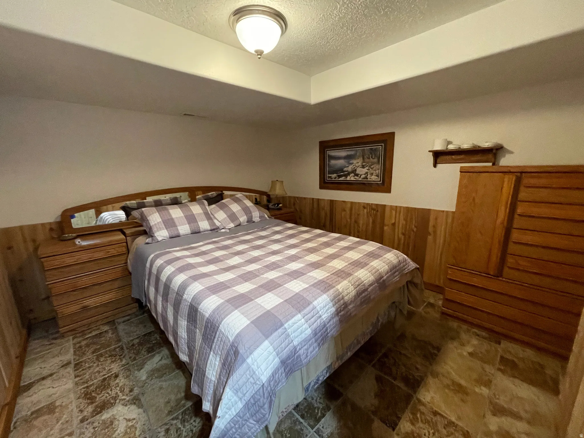 Bedroom with wood walls, wainscoting, a textured ceiling, and dark stone finish floors