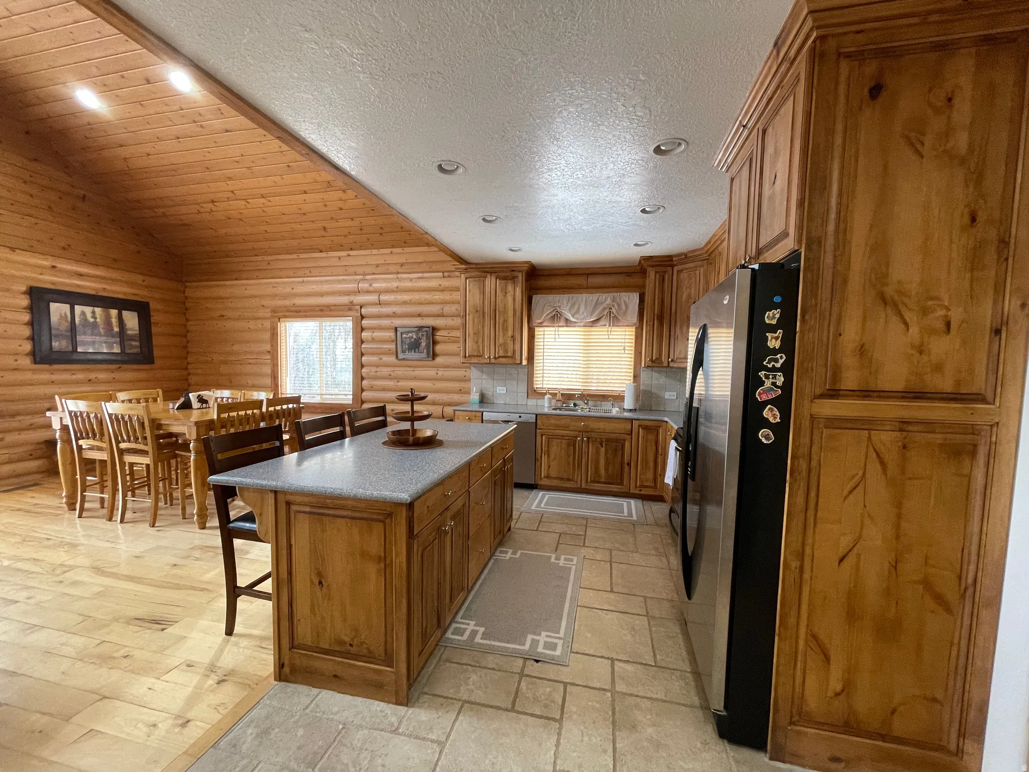 Kitchen featuring wood finish cabinets, rustic walls, stainless steel appliances, a breakfast bar, and a kitchen island