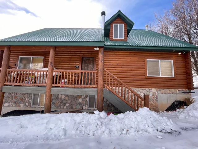 Snow covered rear of property with covered porch, a metal roof, and stone siding