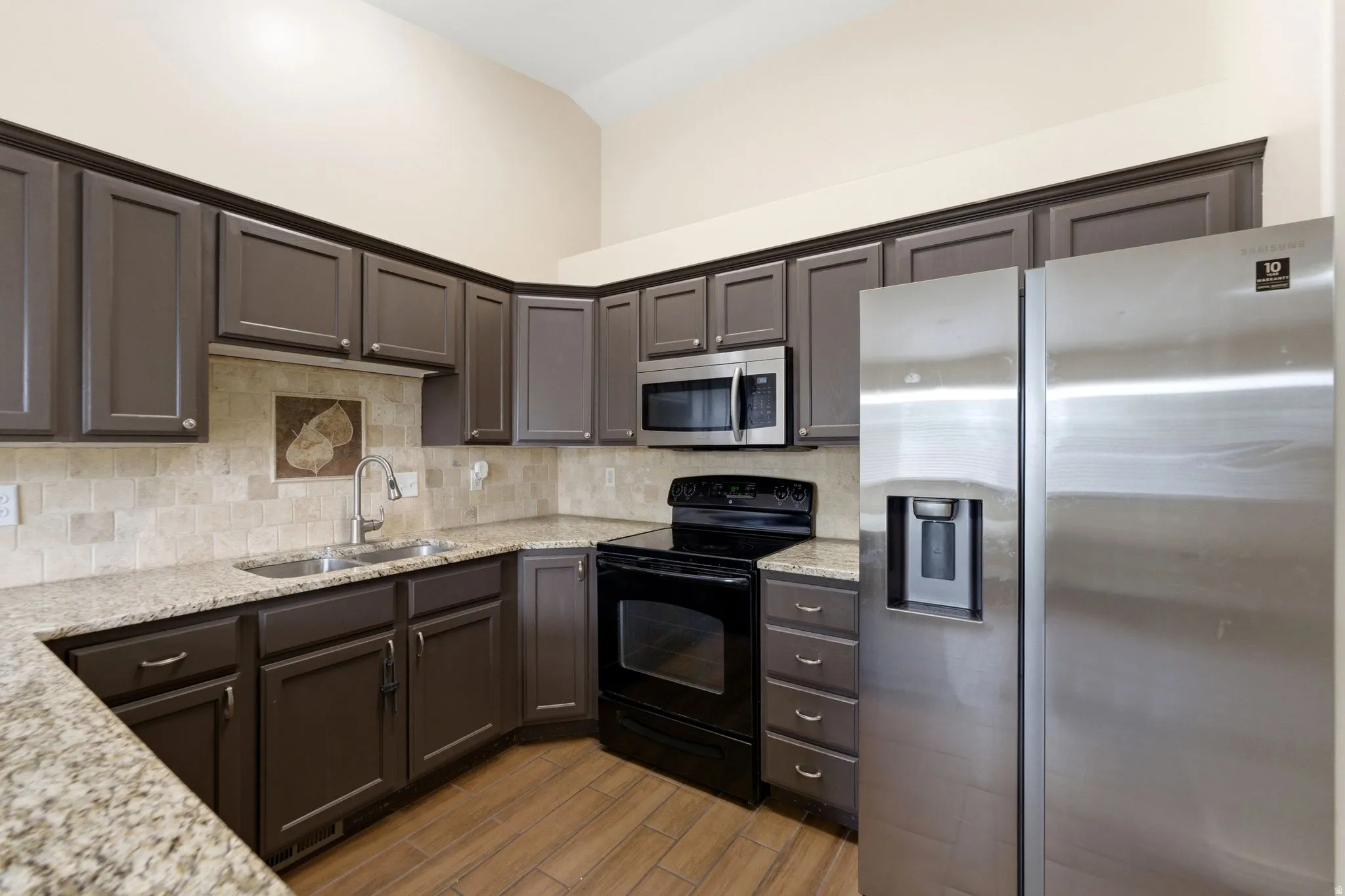 Kitchen with stainless steel appliances, light stone countertops, decorative backsplash, wood finish floors, and dark wood finish cabinetry
