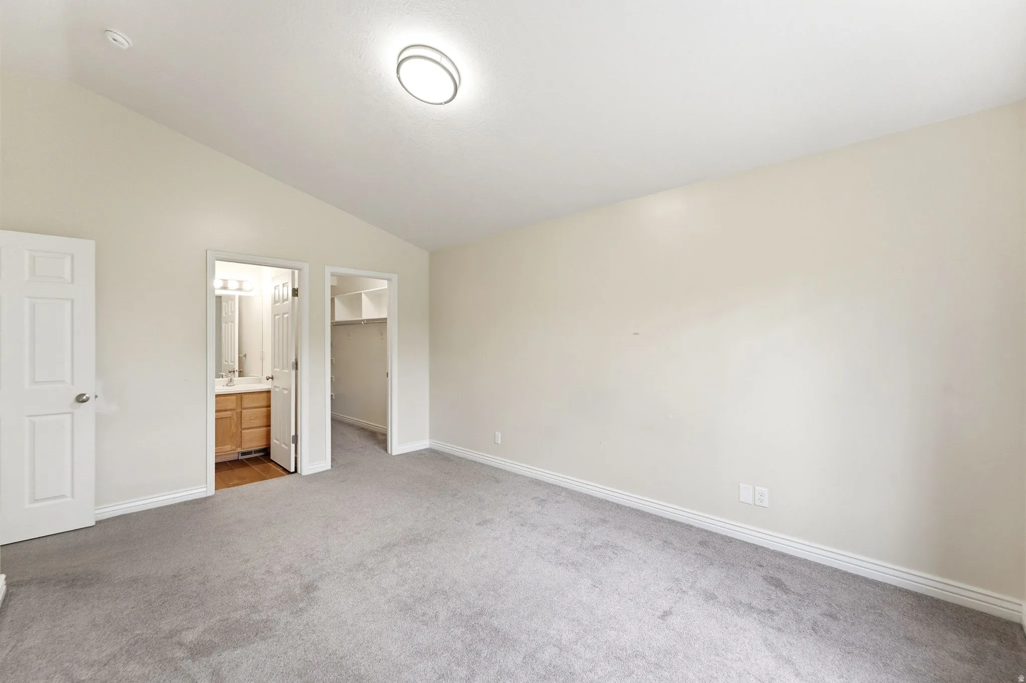 Unfurnished bedroom featuring a walk in closet, carpet floors, vaulted ceiling, and connected bathroom