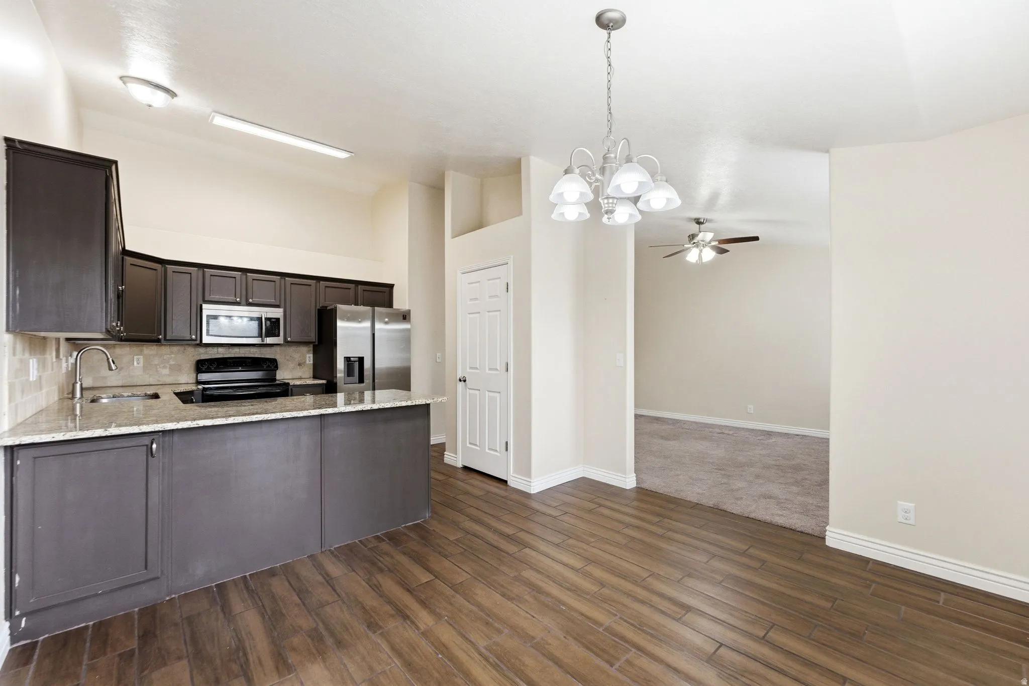 Kitchen with suspended lighting, dark wood finish cabinetry, stainless steel appliances, light stone countertops, and ceiling fan