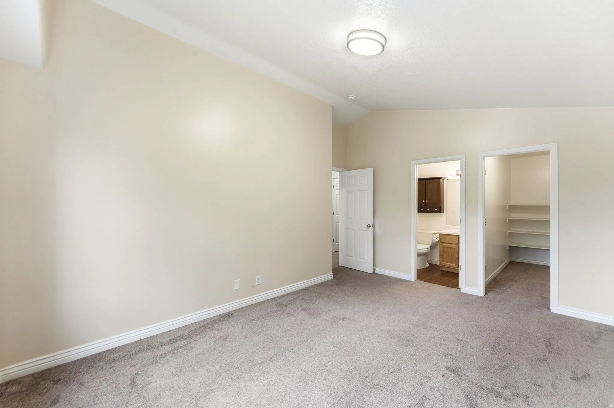 Unfurnished bedroom with a walk in closet, light colored carpet, vaulted ceiling, and ensuite bath
