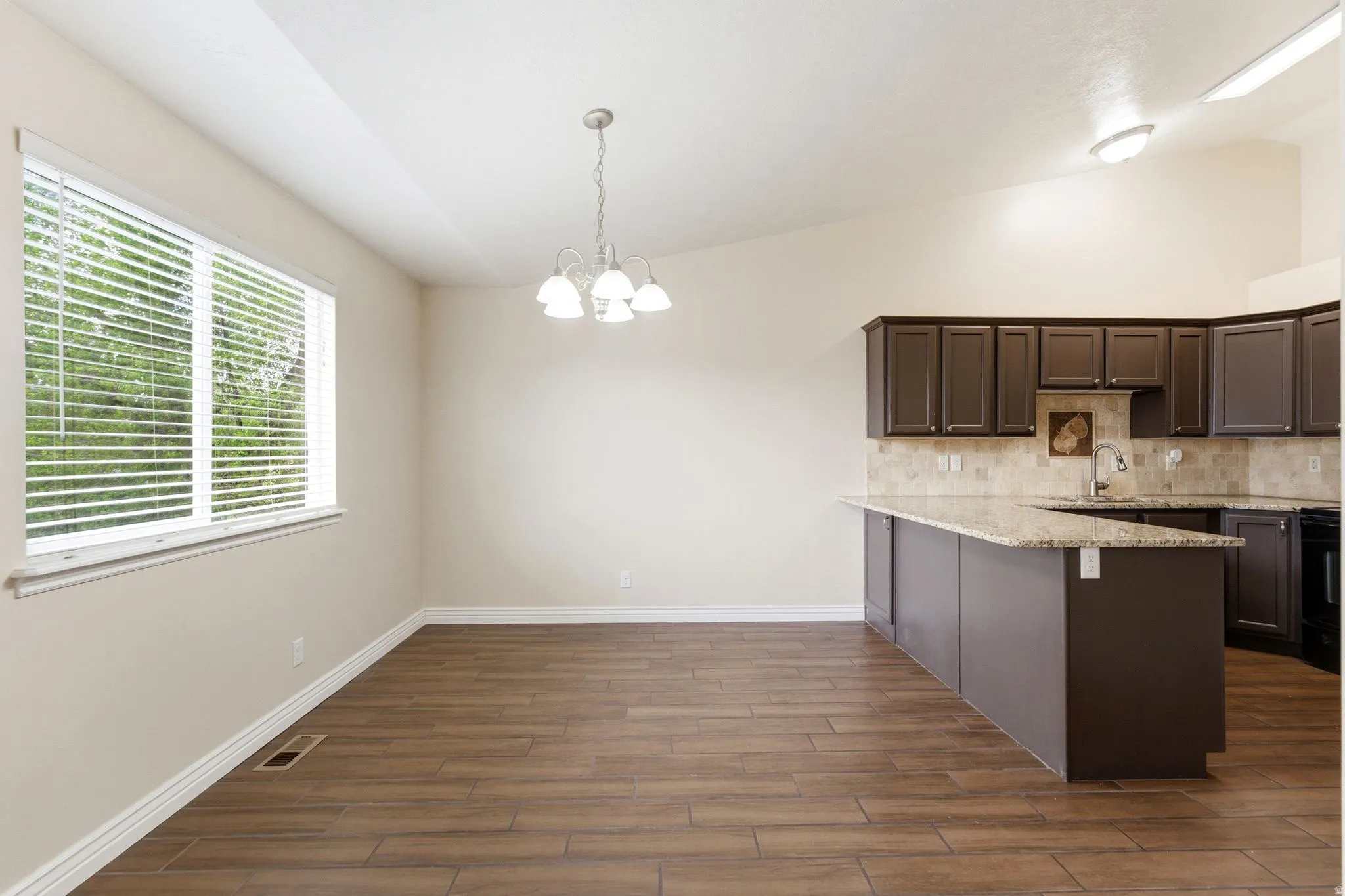 Kitchen with vaulted ceiling, dark wood finish cabinets, a peninsula, hanging lights, and decorative backsplash