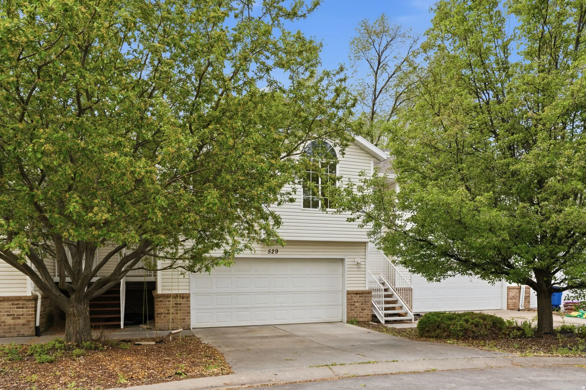 View of property hidden behind natural elements featuring brick siding, concrete driveway, and an attached garage