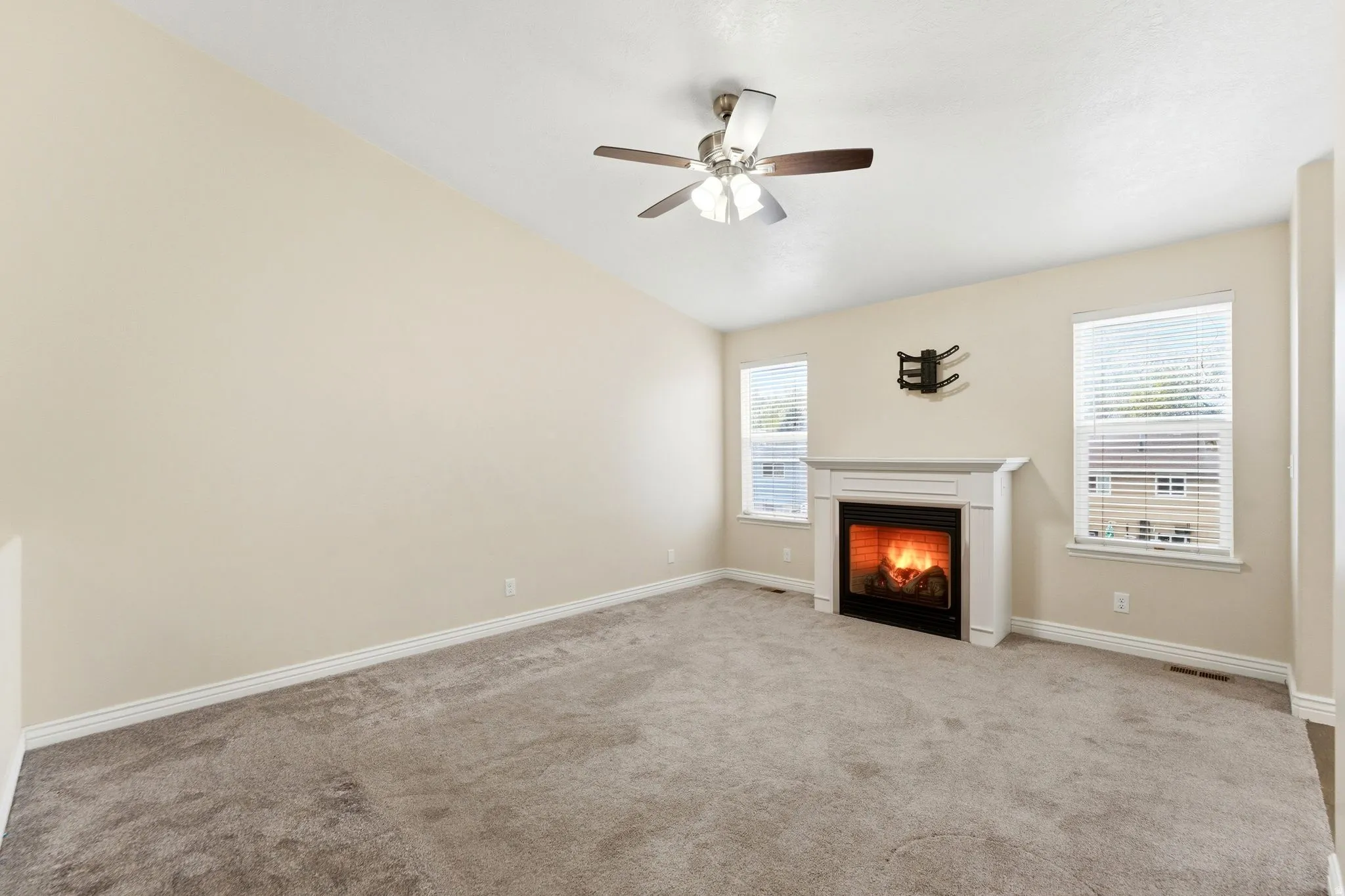 Unfurnished living room featuring a lit fireplace, light colored carpet, ceiling fan, and lofted ceiling