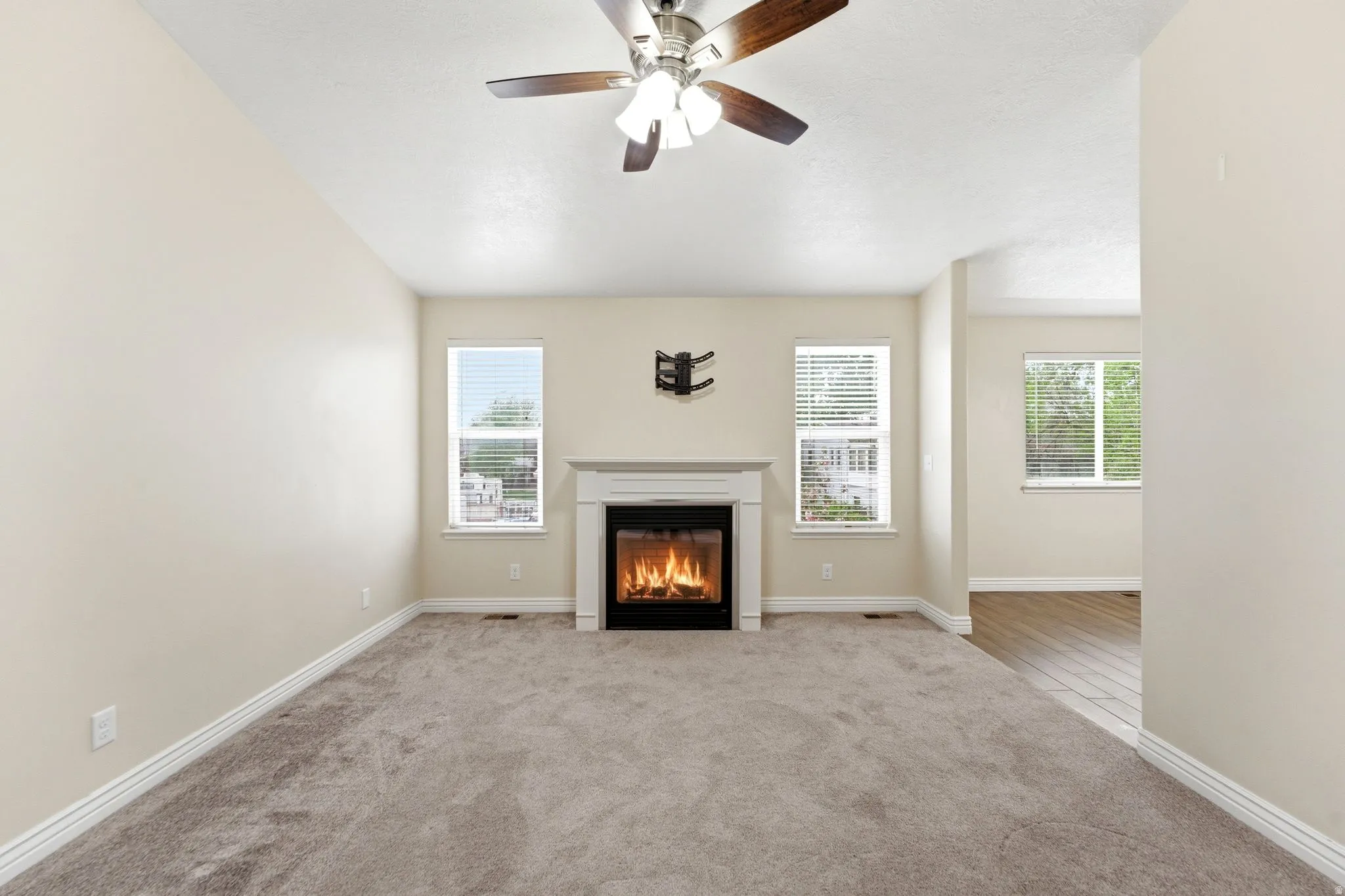 Unfurnished living room with light colored carpet, healthy amount of natural light, a glass covered fireplace, and ceiling fan