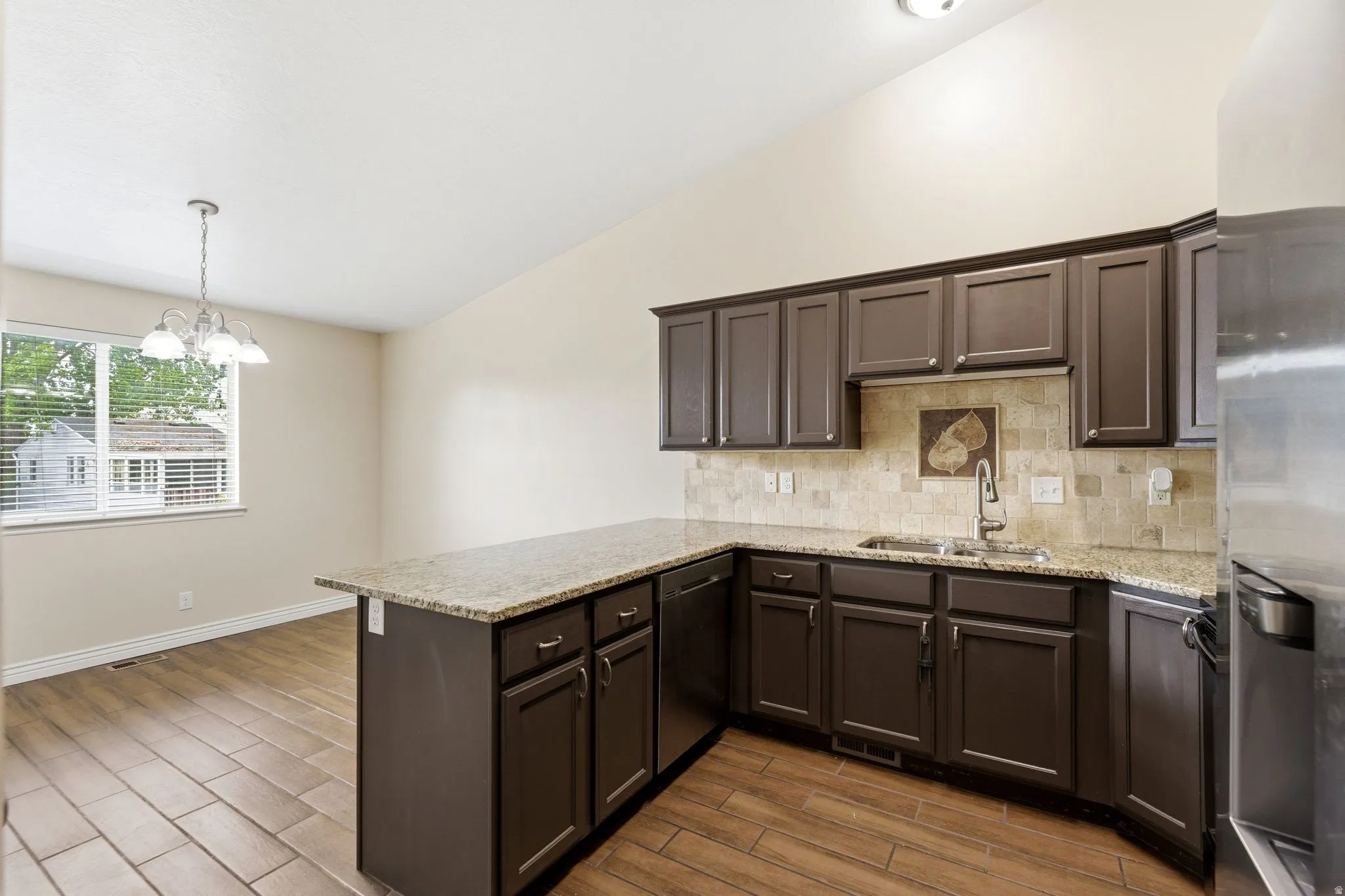 Kitchen featuring a peninsula, lofted ceiling, dark wood finish cabinets, stainless steel appliances, and light stone counters
