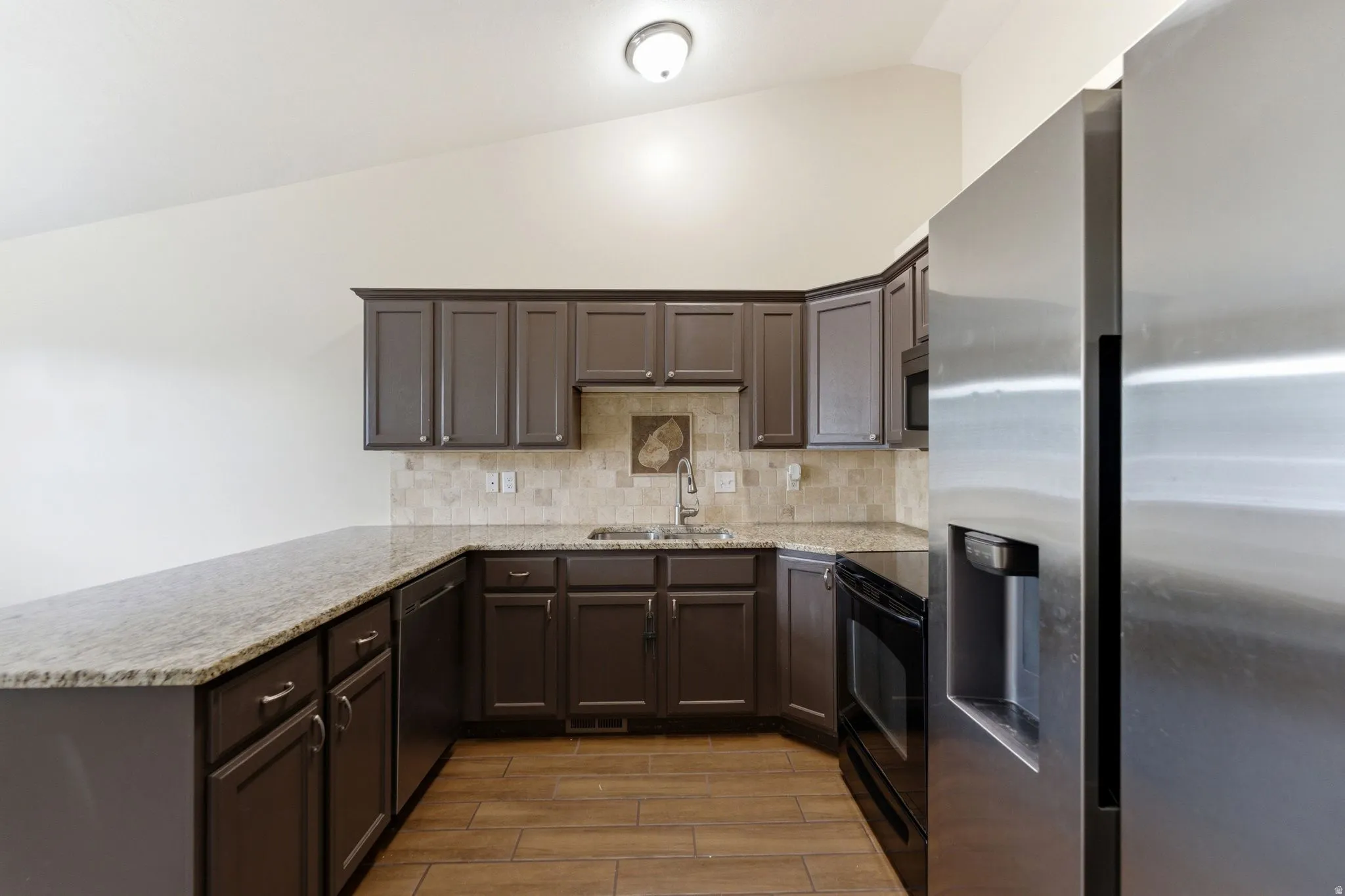 Kitchen featuring stainless steel appliances, vaulted ceiling, dark wood finish cabinets, a peninsula, and wood tiled floors