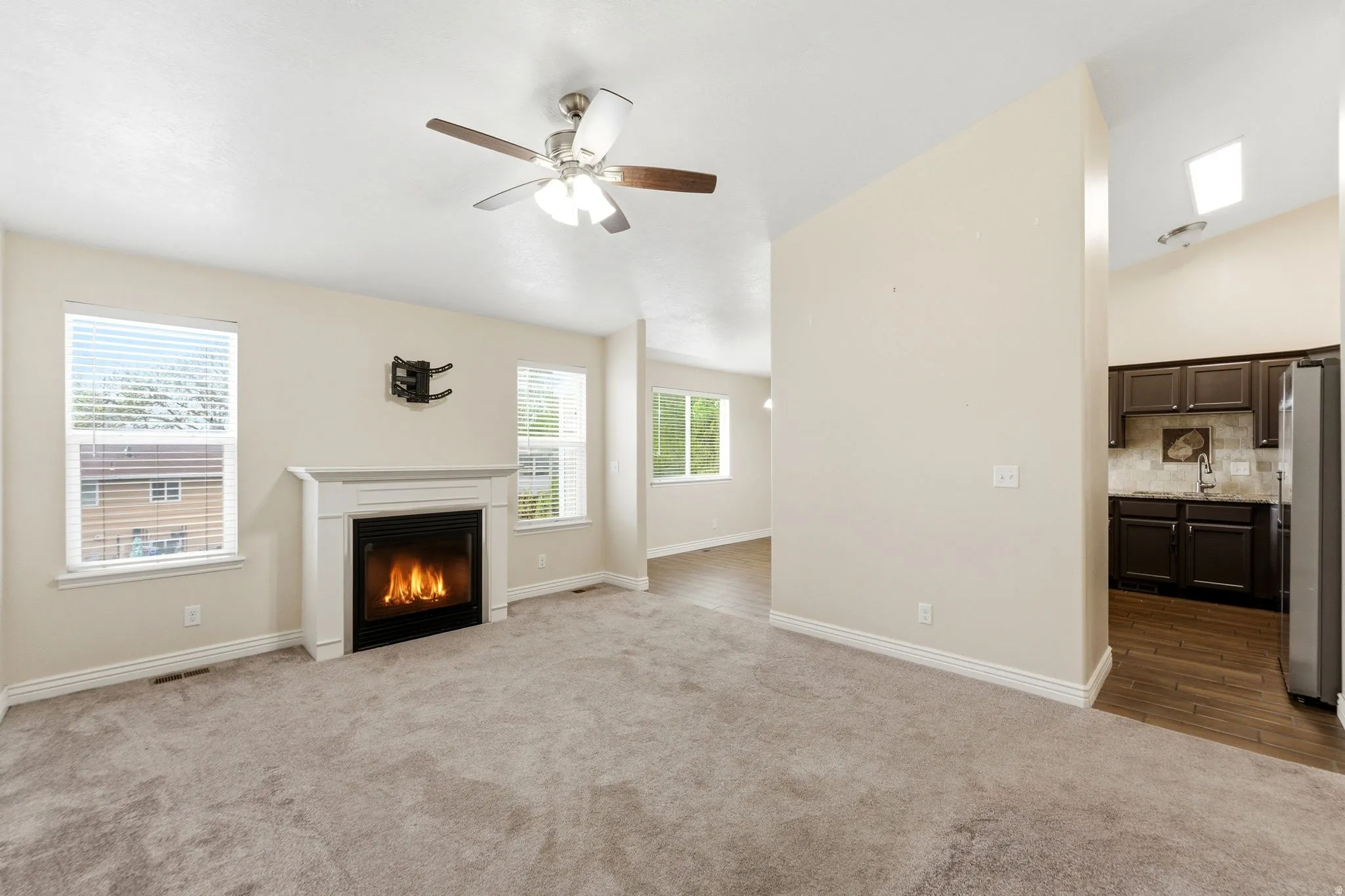 Unfurnished living room featuring dark carpet, ceiling fan, and a glass covered fireplace