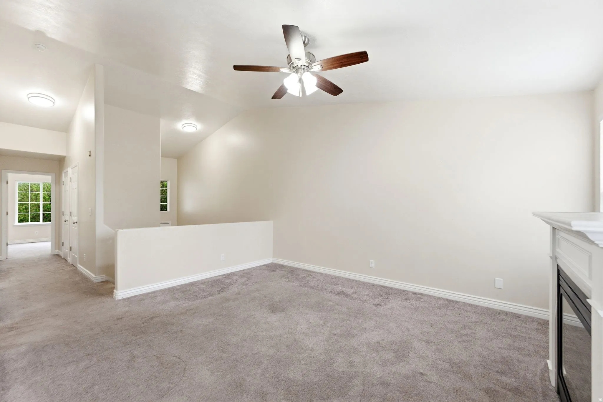 Unfurnished living room with light carpet, ceiling fan, a glass covered fireplace, and lofted ceiling