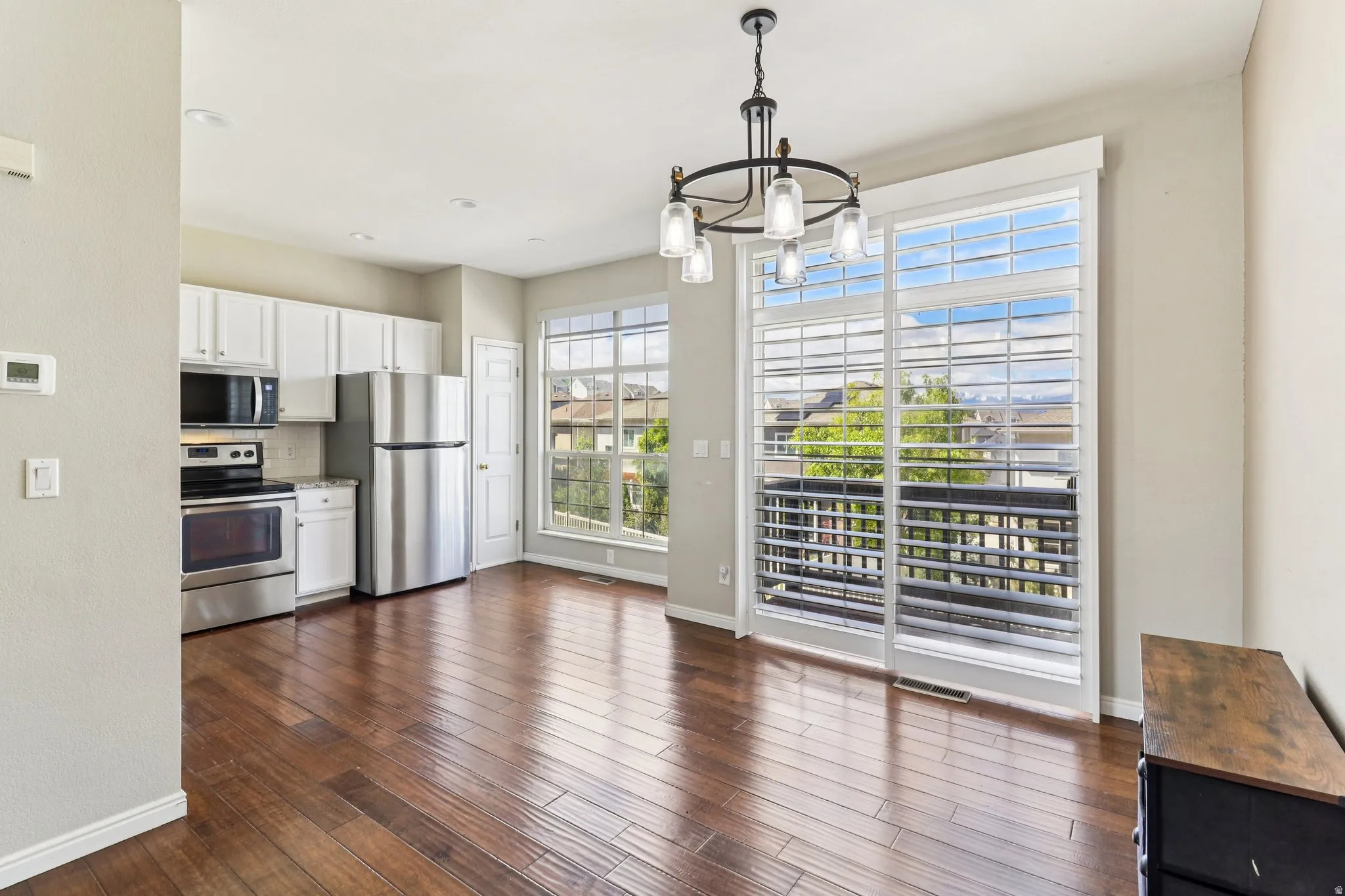 Kitchen featuring white cabinetry, stainless steel appliances, suspended lighting, dark wood-type flooring, and tasteful backsplash