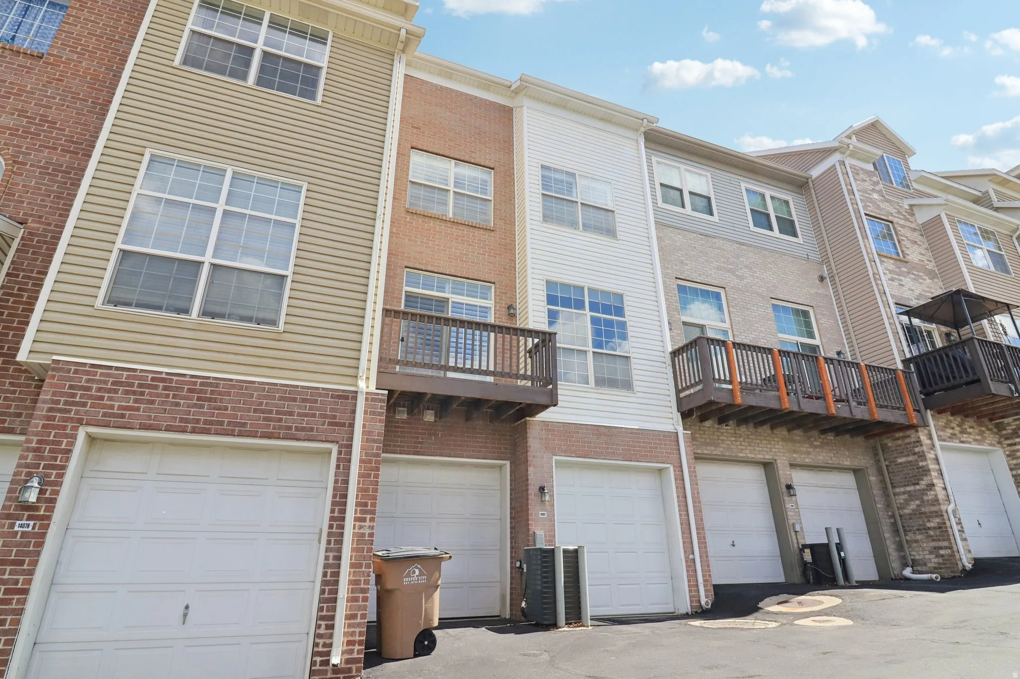 Back of house with brick siding, a balcony, and an attached garage