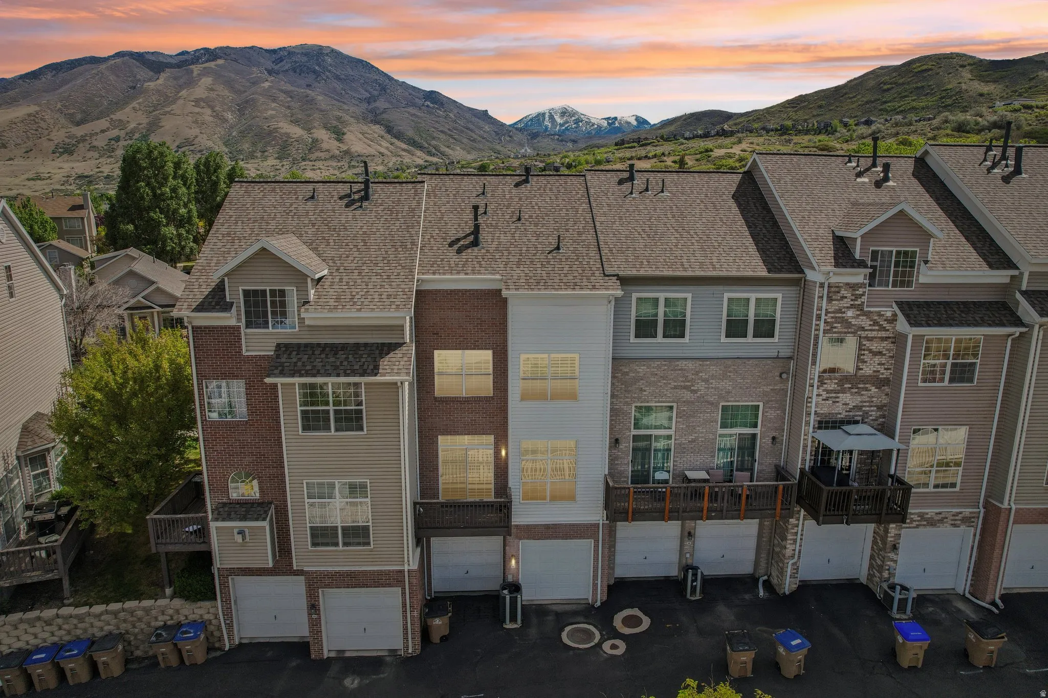 Back of property at dusk with a mountain view, an attached garage, brick siding, and driveway