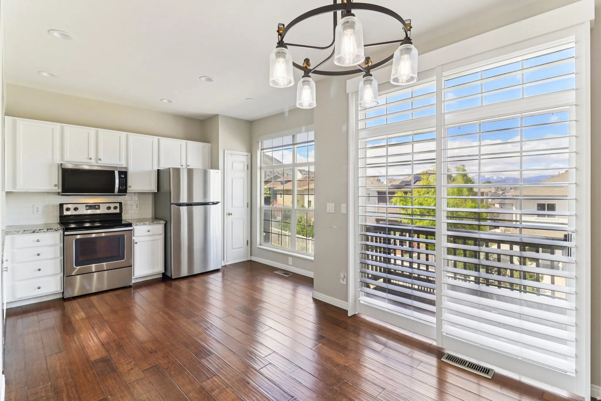 Kitchen with white cabinets, stainless steel appliances, tasteful backsplash, dark wood finished floors, and a chandelier