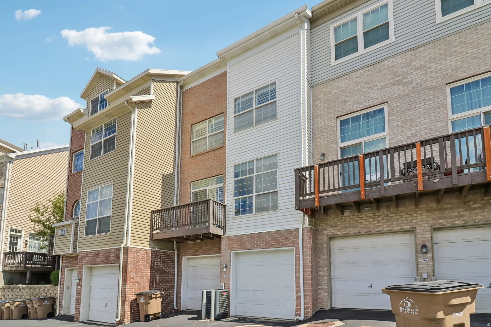Back of property with a balcony, brick siding, an attached garage, and driveway
