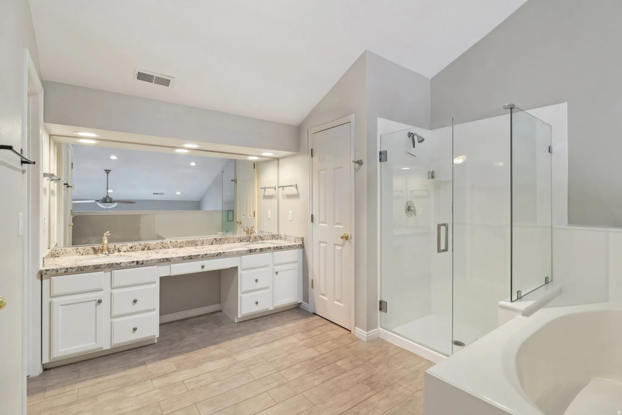 Bathroom featuring double vanity, a bath, light wood-style flooring, a stall shower, and vaulted ceiling