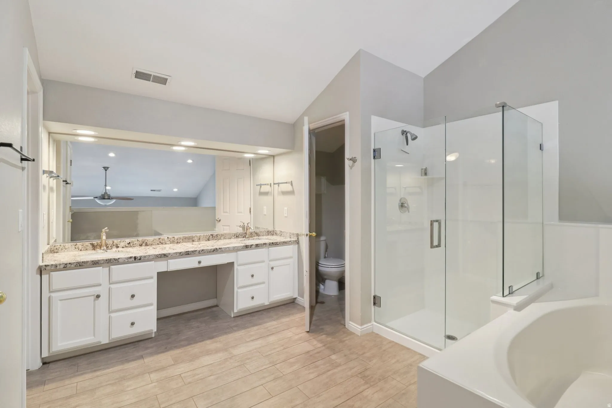 Full bath featuring double vanity, a garden tub, light wood finished floors, a stall shower, and vaulted ceiling