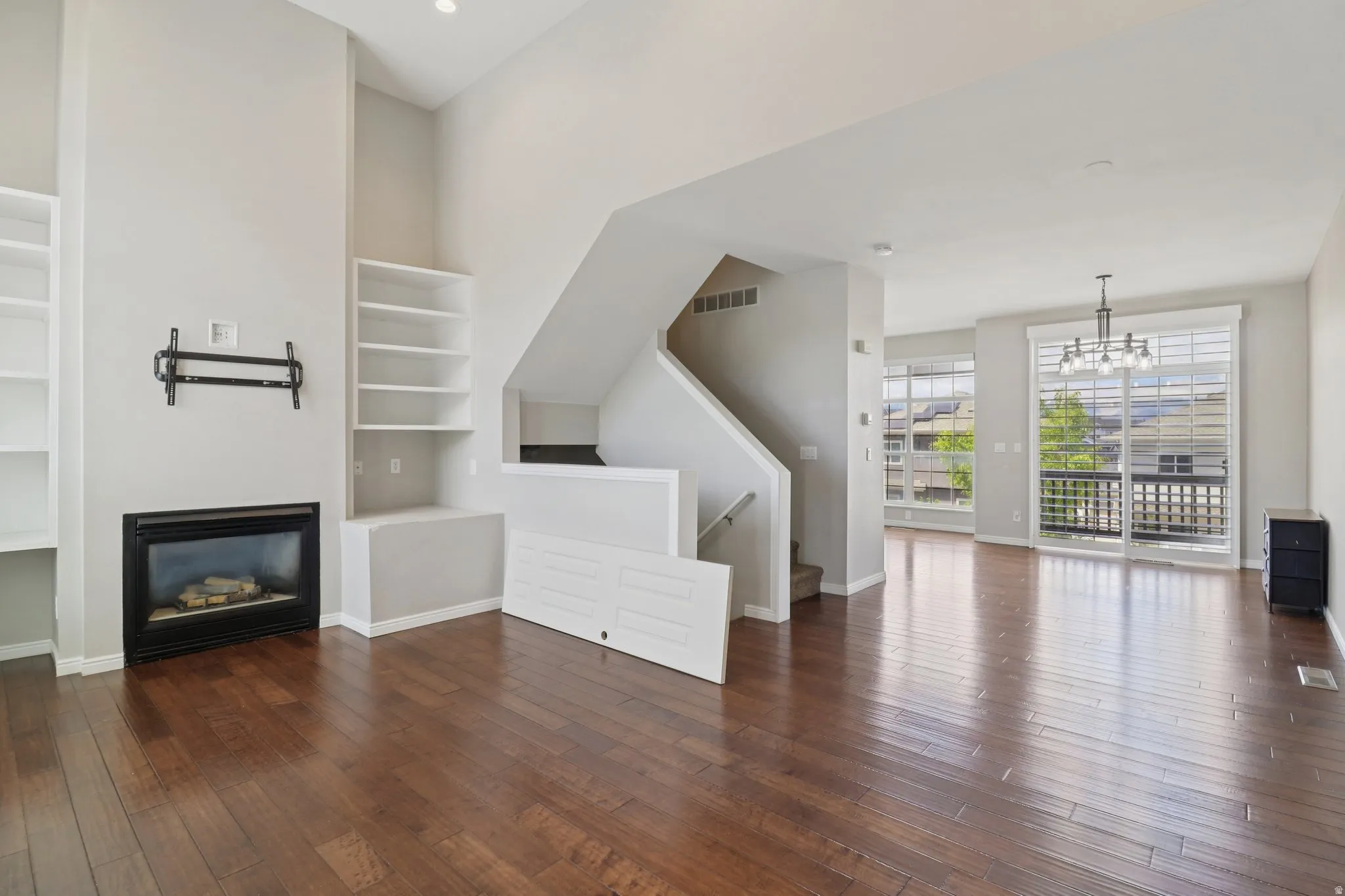 Unfurnished living room with dark wood-type flooring, suspended lighting, a glass covered fireplace, and built in features