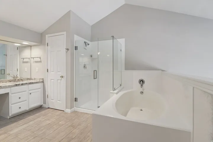 Bathroom featuring vanity, a stall shower, a bath, light wood-style floors, and lofted ceiling