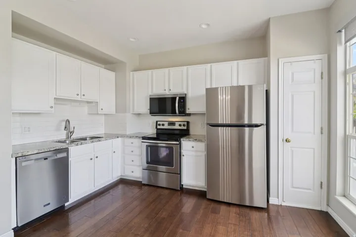 Kitchen with stainless steel appliances, white cabinets, and dark wood-style flooring
