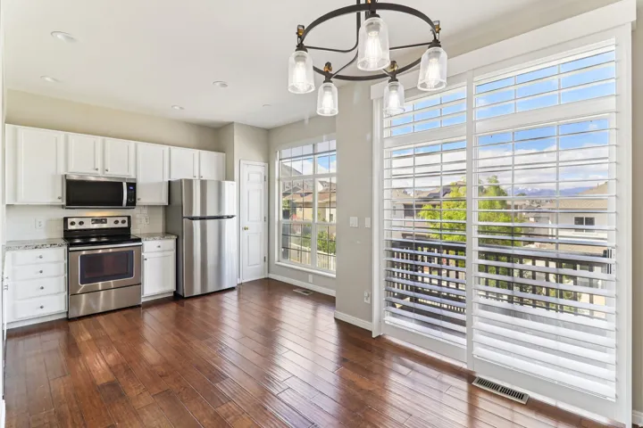 Kitchen with white cabinets, stainless steel appliances, tasteful backsplash, dark wood finished floors, and a chandelier